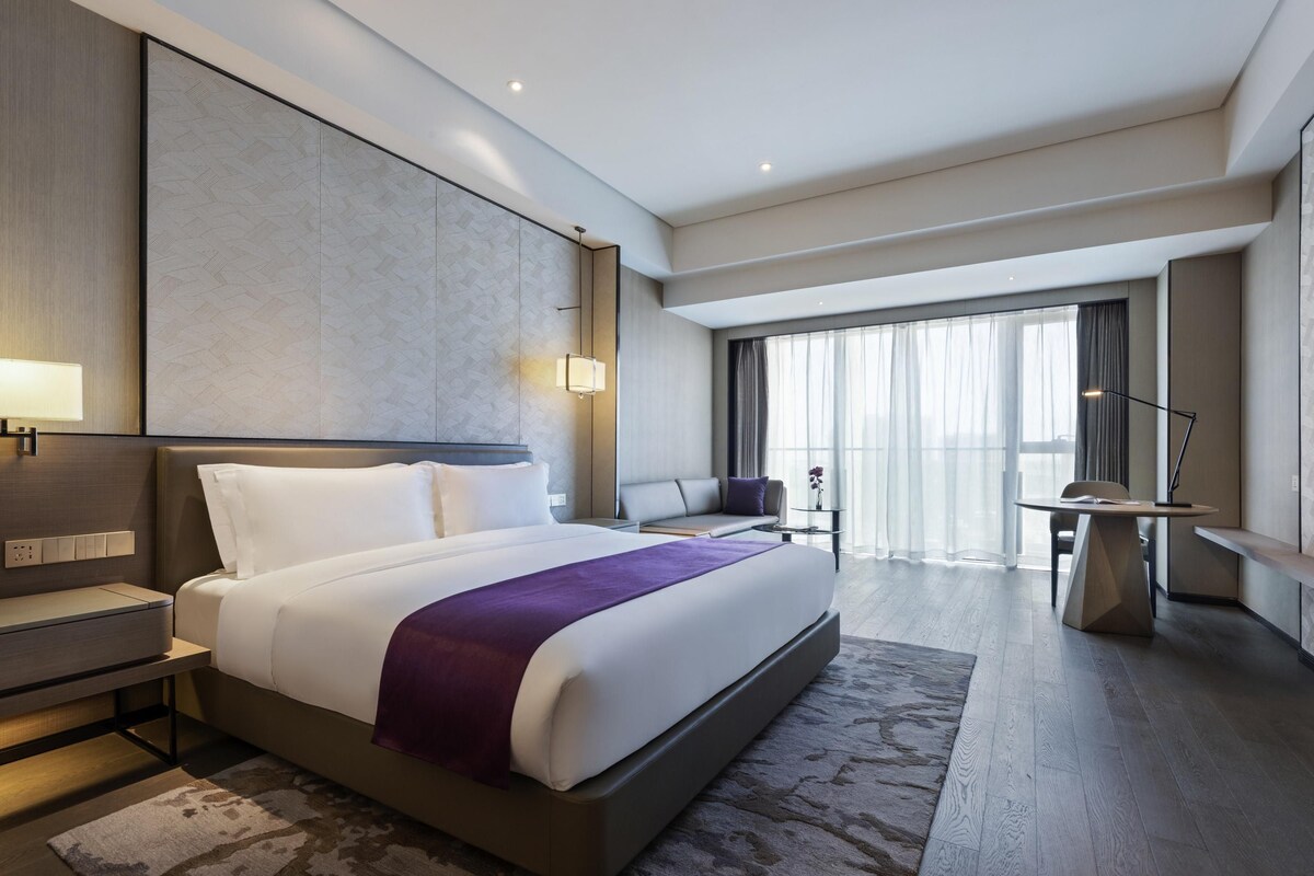 Una habitación de hotel moderna con una cama grande, mesitas de noche, un escritorio y vistas a la ciudad.