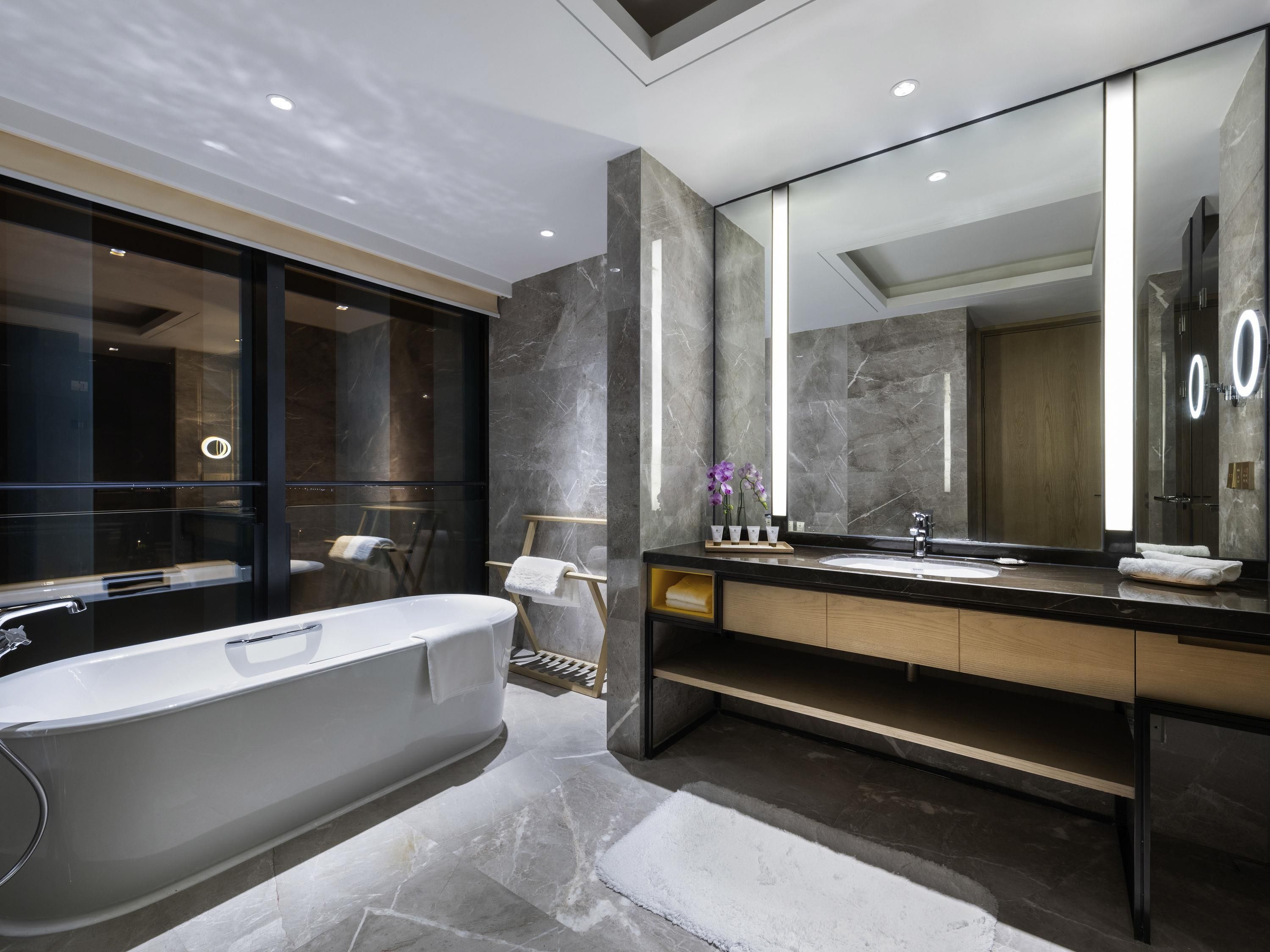 A modern bathroom with a freestanding bathtub, a large mirror, and marble flooring.