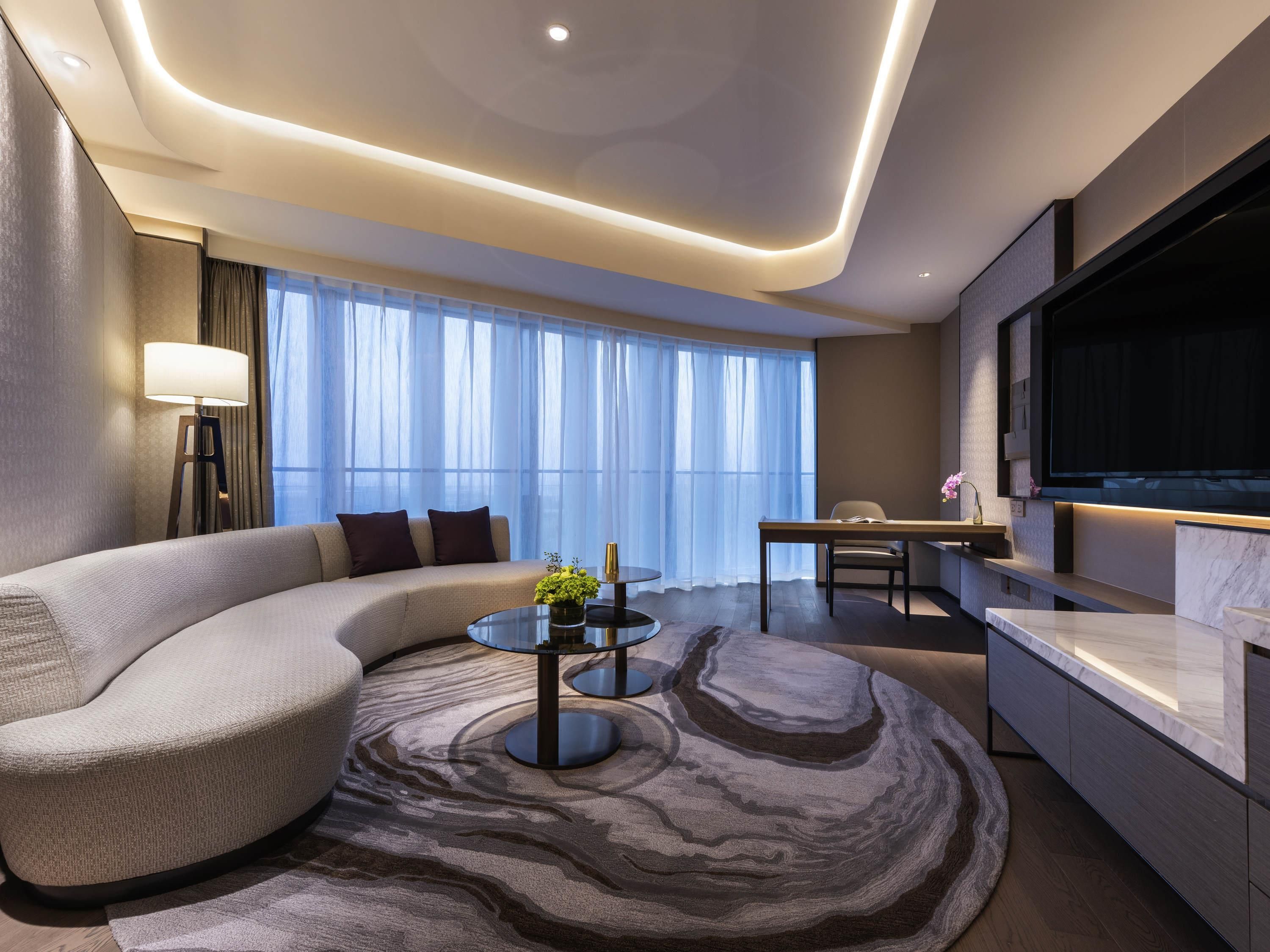 A modern living room with a curved sofa, a round coffee table, and a TV mounted on the wall.