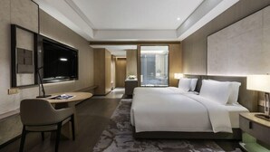 Et moderne hotelværelse med en stor seng, et skrivebord, et fjernsyn og et badeværelse, der kan ses gennem en åben dør.