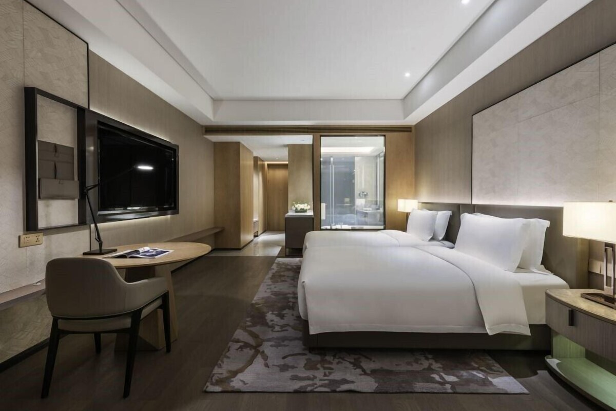 A modern hotel room with a large bed, a desk, a TV, and a bathroom visible through an open door.