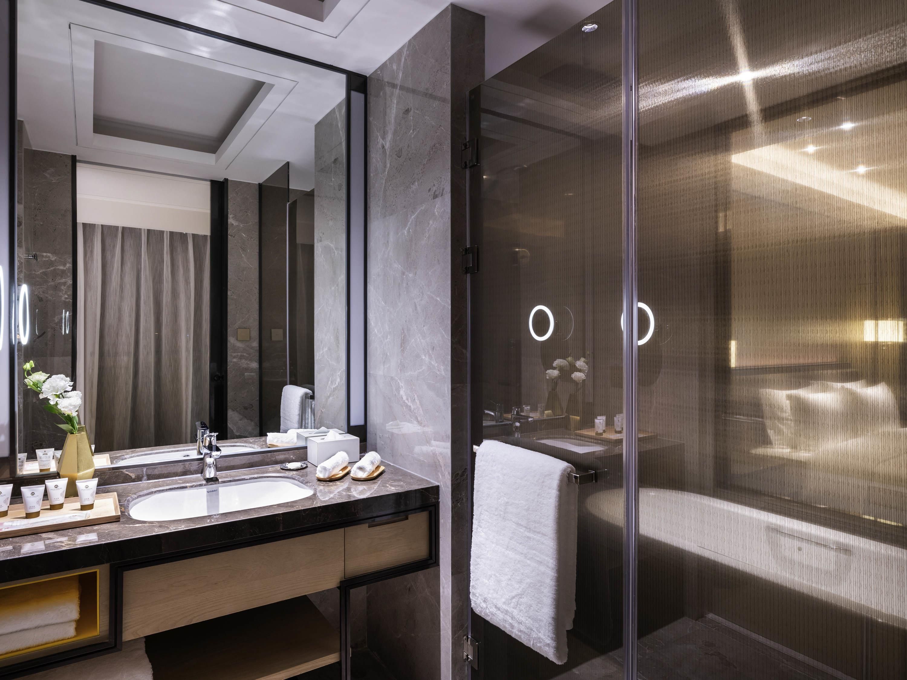 A modern bathroom with a large mirror, two sinks, a shower area, and a towel rack.