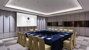 Una sala de conferencias con una larga mesa, sillas, una pantalla de proyector y un amplio ventanal.