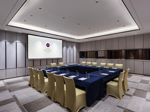 Una sala de conferencias con una larga mesa, sillas, una pantalla de proyector y un amplio ventanal.