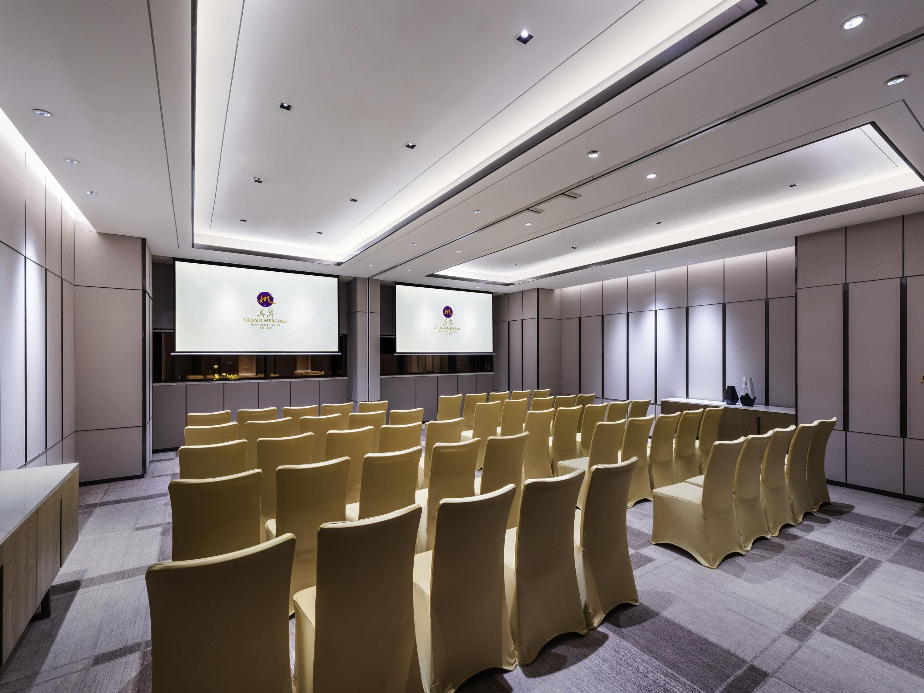 A conference room with rows of chairs, two large screens, and a modern ceiling design.