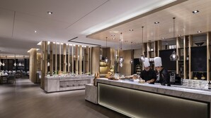 Un interior de restaurante moderno con mostrador de mármol, detalles de madera e iluminación colgante.