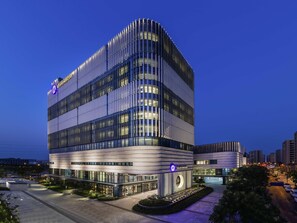 A modern hotel with a curved facade, multiple floors, and a prominent circular logo. - Grand Mercure Shanghai Lingang (Shanghai)