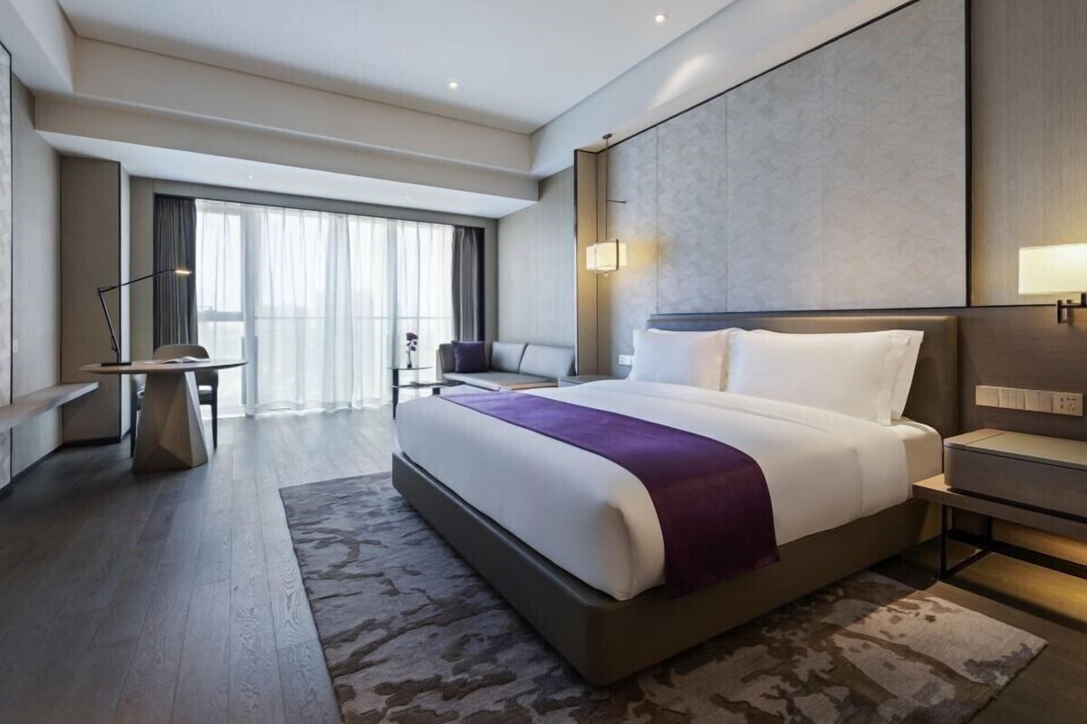 A modern hotel room with a large bed, a desk, and a seating area.