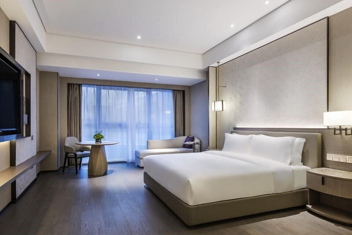 A modern hotel room with a large bed, a desk, a chair, and a TV.