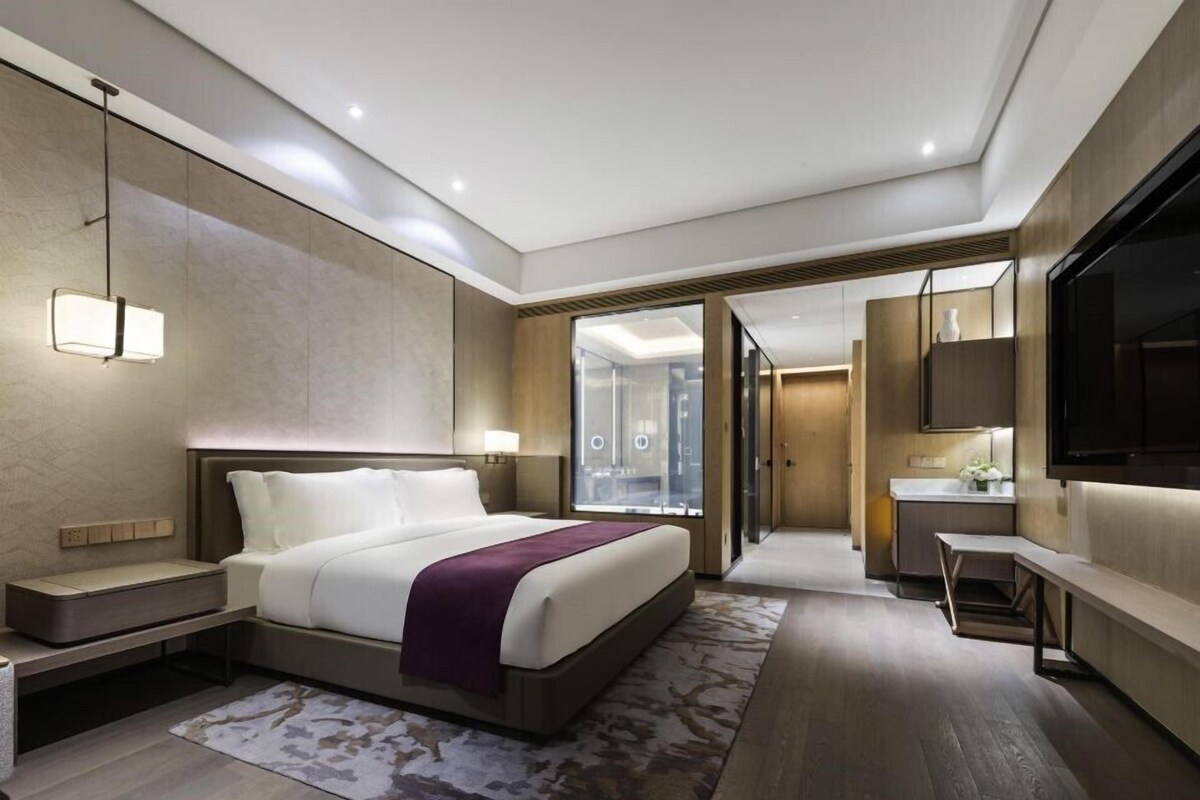 A modern hotel room with a large bed, bedside tables, a desk, and a TV.