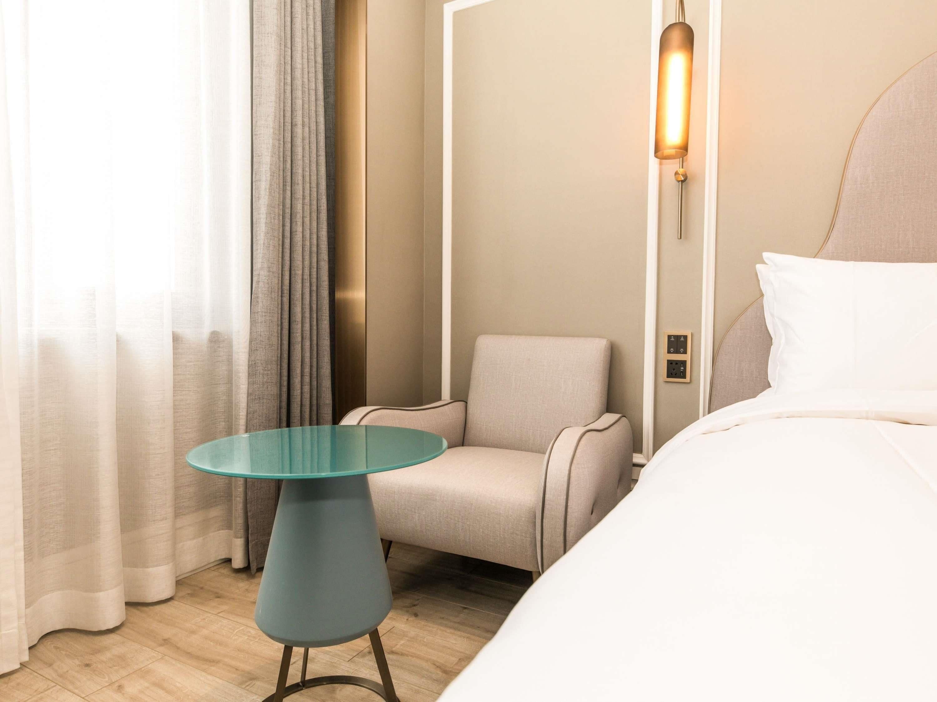 Ett hotellrum med en säng, ett runt bord, en stol och en väggmonterad lampa.