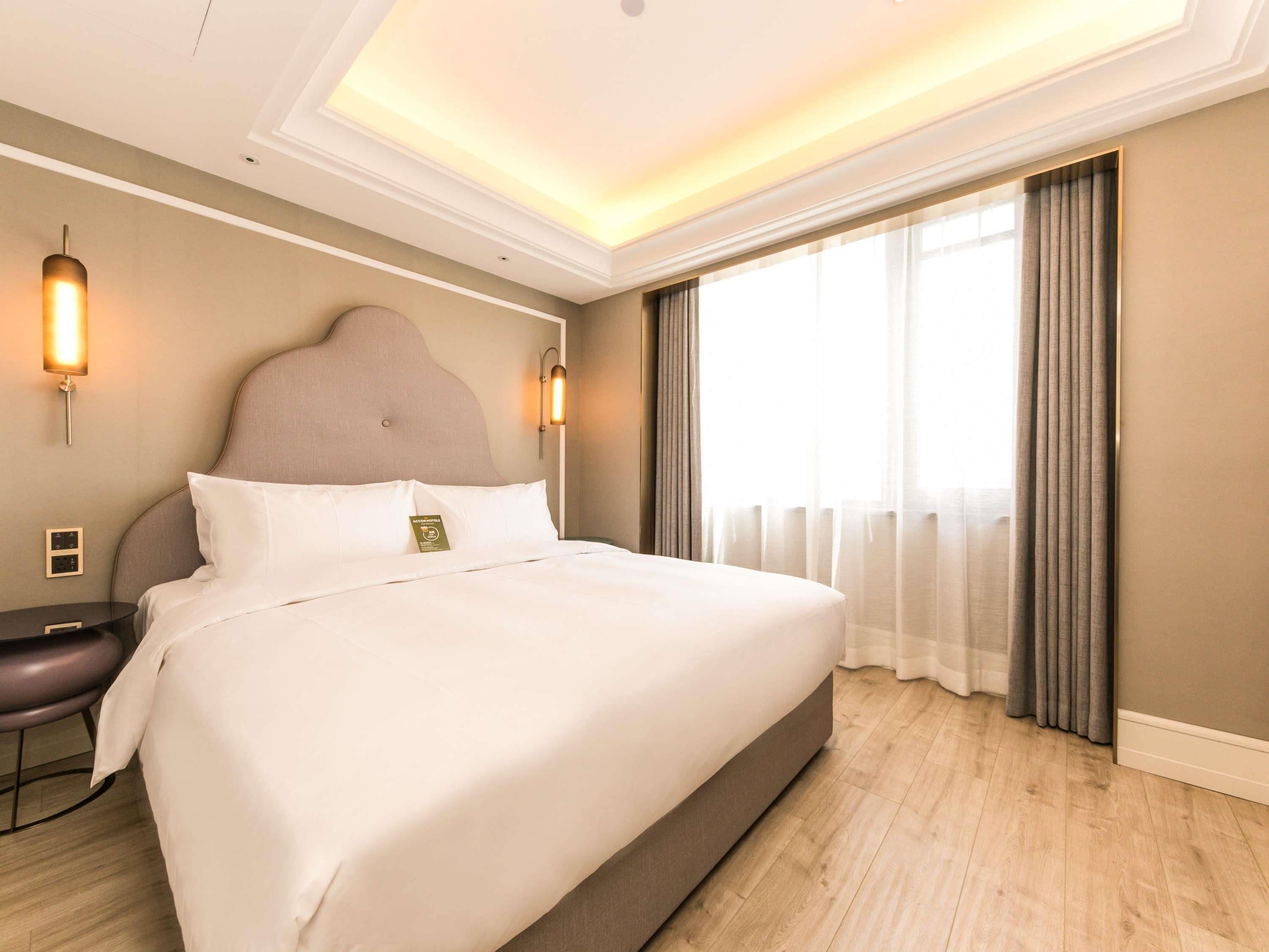 A hotel room with a large bed, a bedside table, a lamp, and a window with curtains.