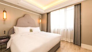 Habitación de hotel con una cama grande, una mesita de noche, una lámpara y una ventana con cortinas.