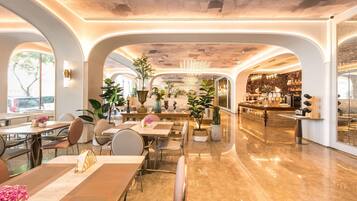 Un amplio vestíbulo de hotel con un bar central, varias zonas de estar y grandes ventanales que dejan entrar luz natural.