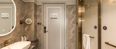 A modern bathroom with a marble sink, a large mirror, a door with a towel rack, and a glass shower enclosure.