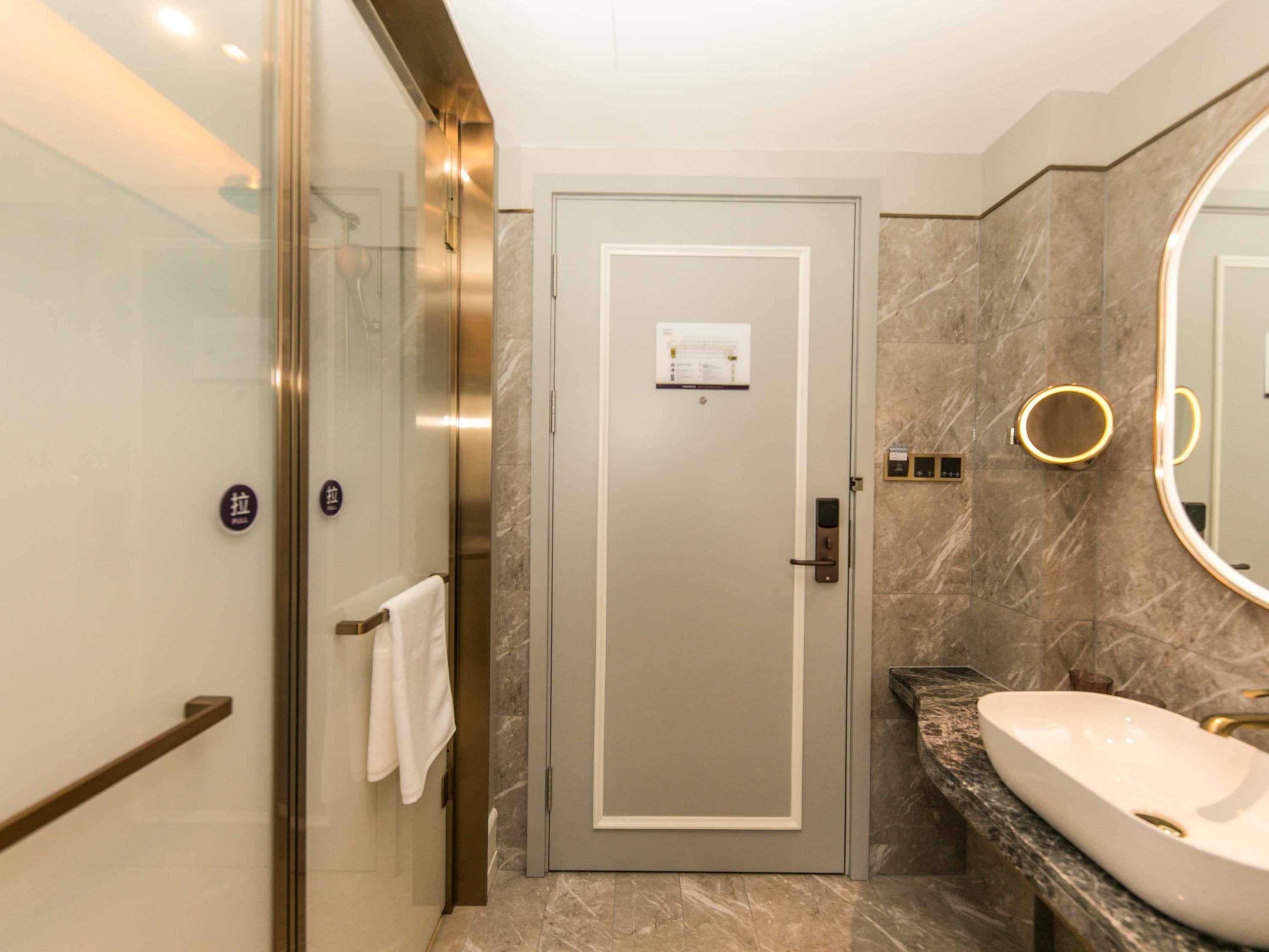A modern bathroom with a glass-enclosed shower, a marble-tiled floor, a sink with a gold faucet, and a large mirror with a gold frame.