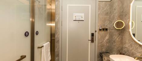 A modern bathroom with a glass-enclosed shower, a marble-tiled floor, a sink with a gold faucet, and a large mirror with a gold frame.
