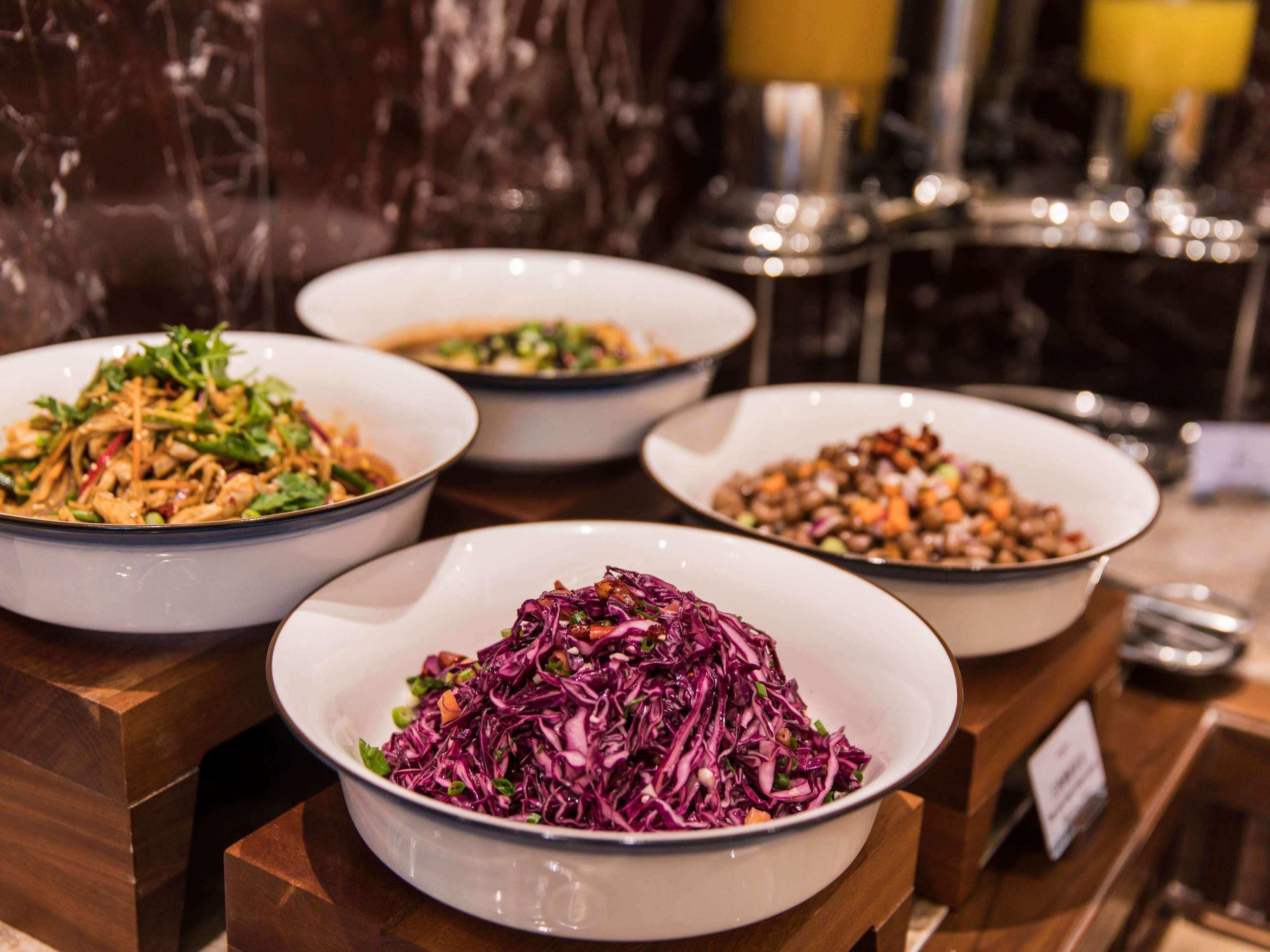 A buffet with various dishes including a bowl of red cabbage salad, a bowl of mixed vegetables, and a bowl of noodles.