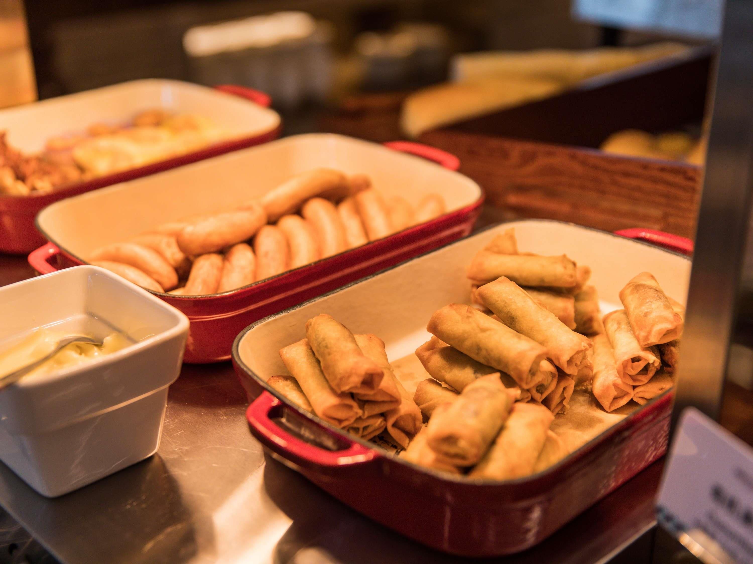 A buffet table with several dishes, including a red container with spring rolls and a white bowl with a sauce.
