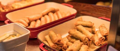 A buffet table with several dishes, including a red container with spring rolls and a white bowl with a sauce.