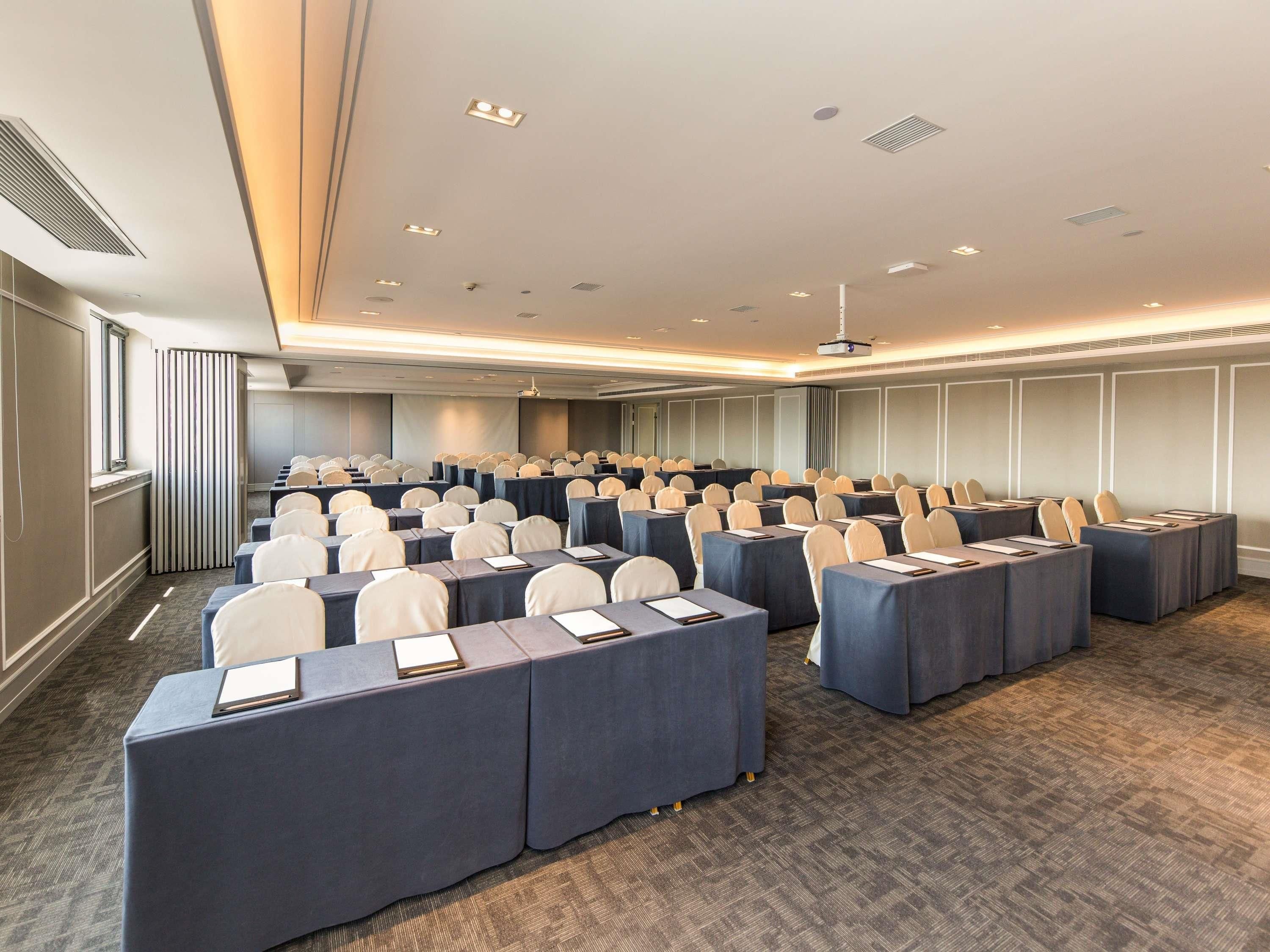 A conference room with rows of tables, chairs, and a projector screen.