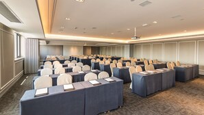 Un salón de conferencias con filas de mesas, sillas y una pantalla para proyector.