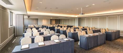 A conference room with rows of tables, chairs, and a projector screen.