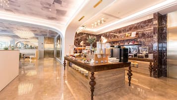 Un moderno vestíbulo de hotel con una recepción de mármol, una barra de café y una zona de estar con vistas a la ciudad.