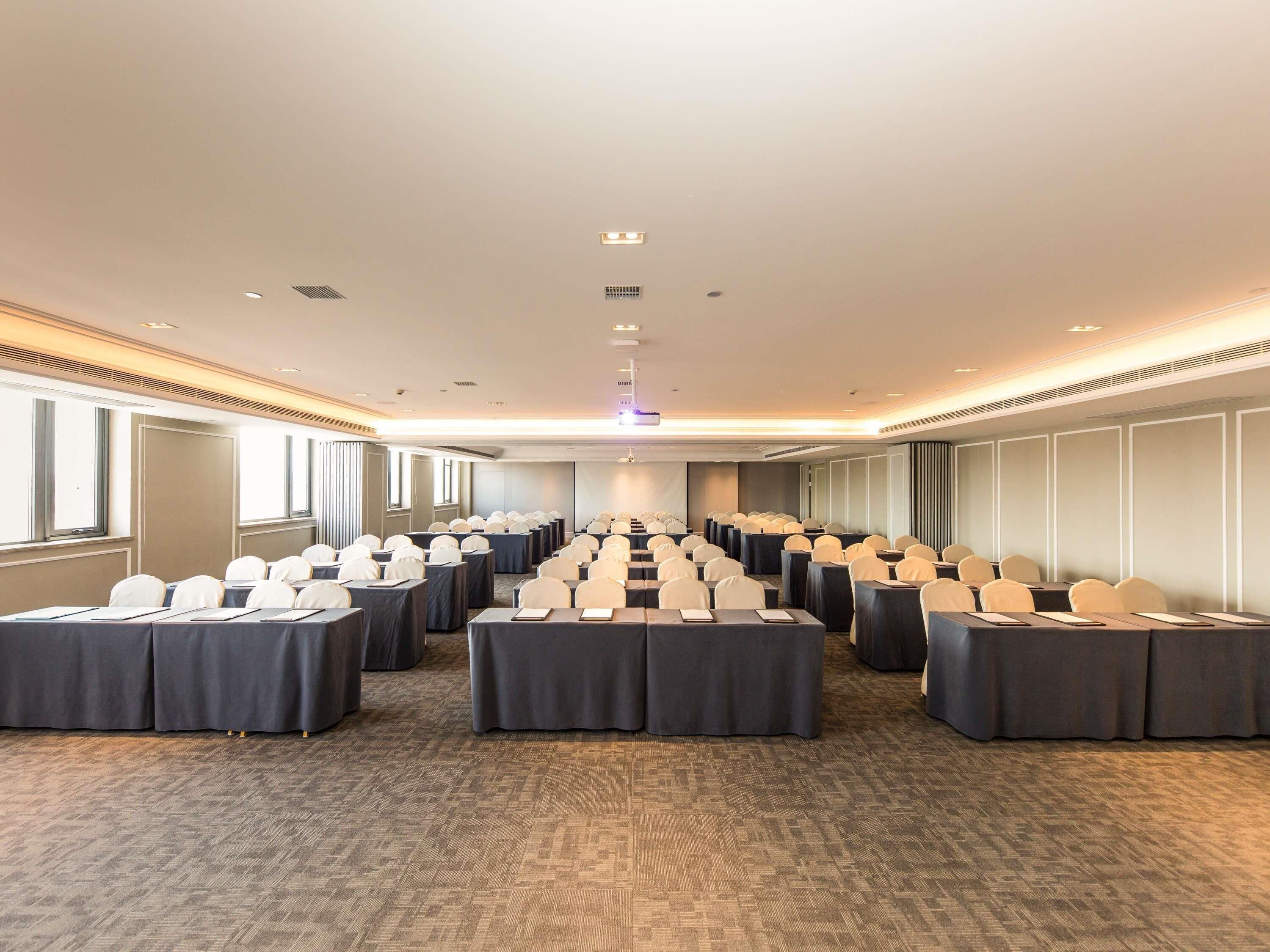 A conference room with rows of tables and chairs, large windows, and a carpeted floor.