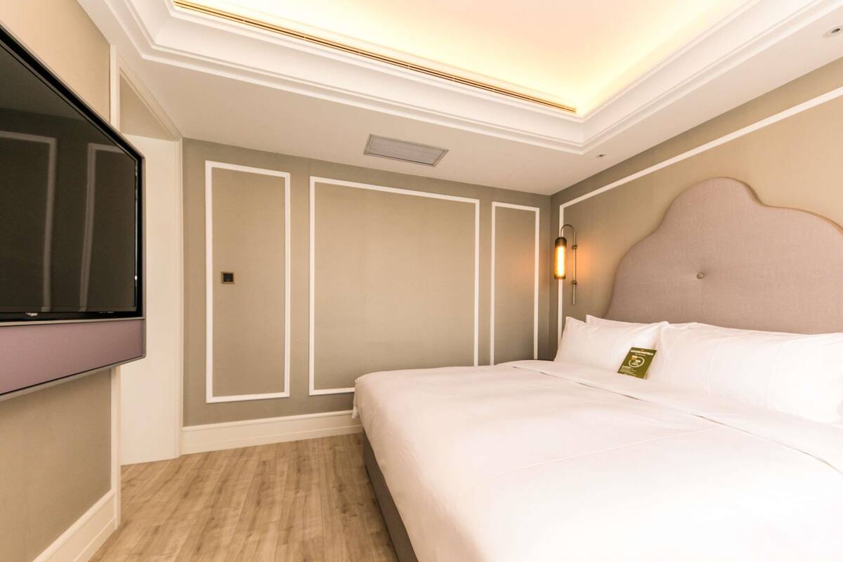 Quarto de hotel com cama, televisão de tela plana na parede e luminária sobre a cama.