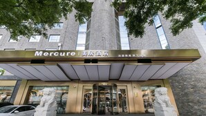 A hotel entrance with a modern facade, large glass windows, and two stone lion statues at the base. - Mercure Xian City Centre (Xi'an)