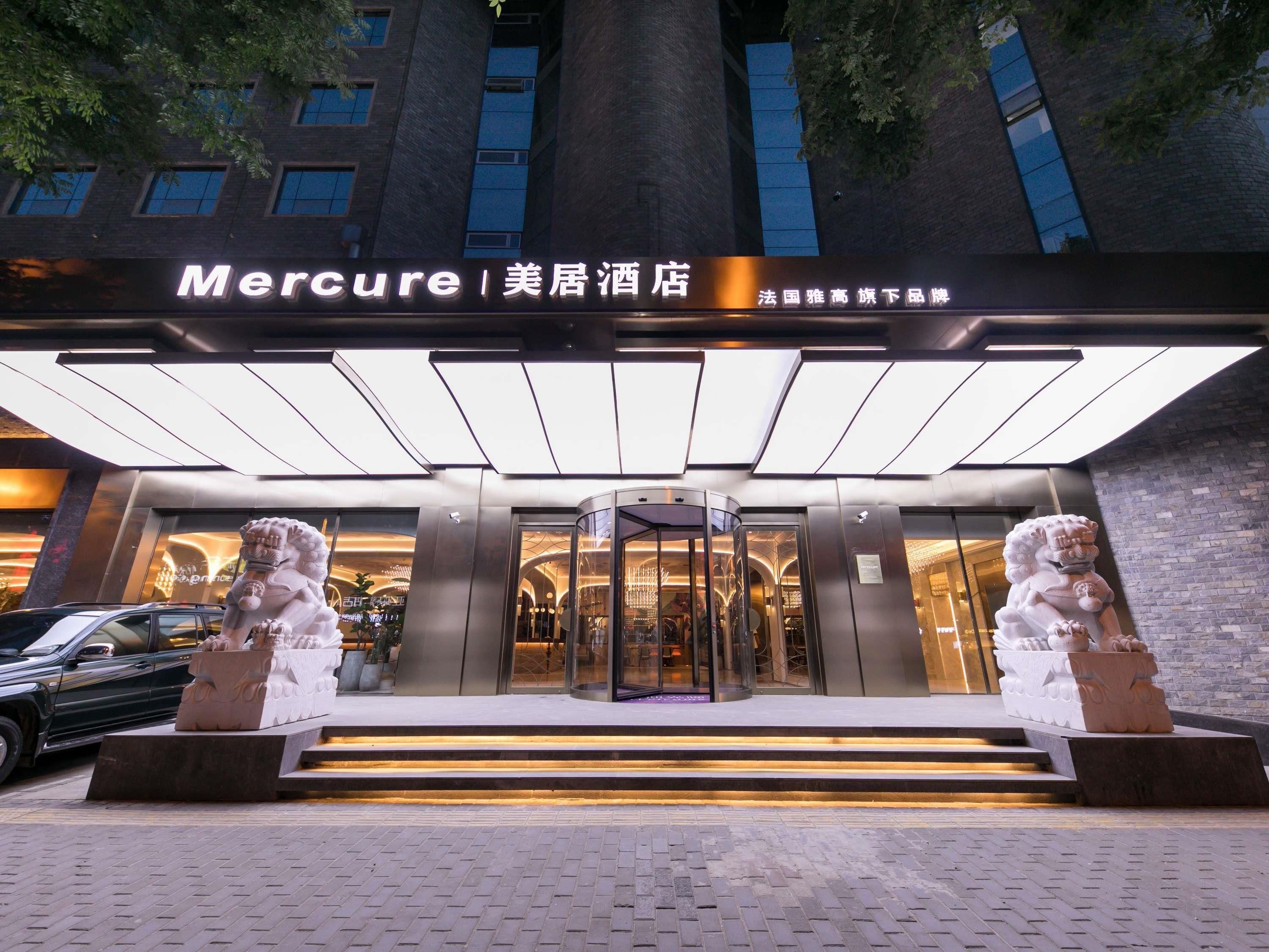 L’entrée d’un hôtel, avec une façade moderne, une porte tournante et deux statues de lions à la base.