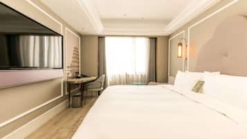 A hotel room with a large bed, a desk with a chair, a TV, and a window with curtains.