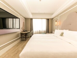 Una habitación de hotel con una cama grande, un escritorio con silla, televisor y ventana con cortinas.