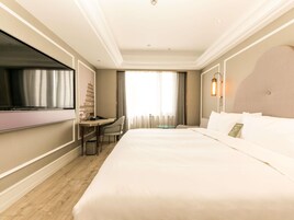 A hotel room with a large bed, a desk with a chair, a TV, and a window with curtains.