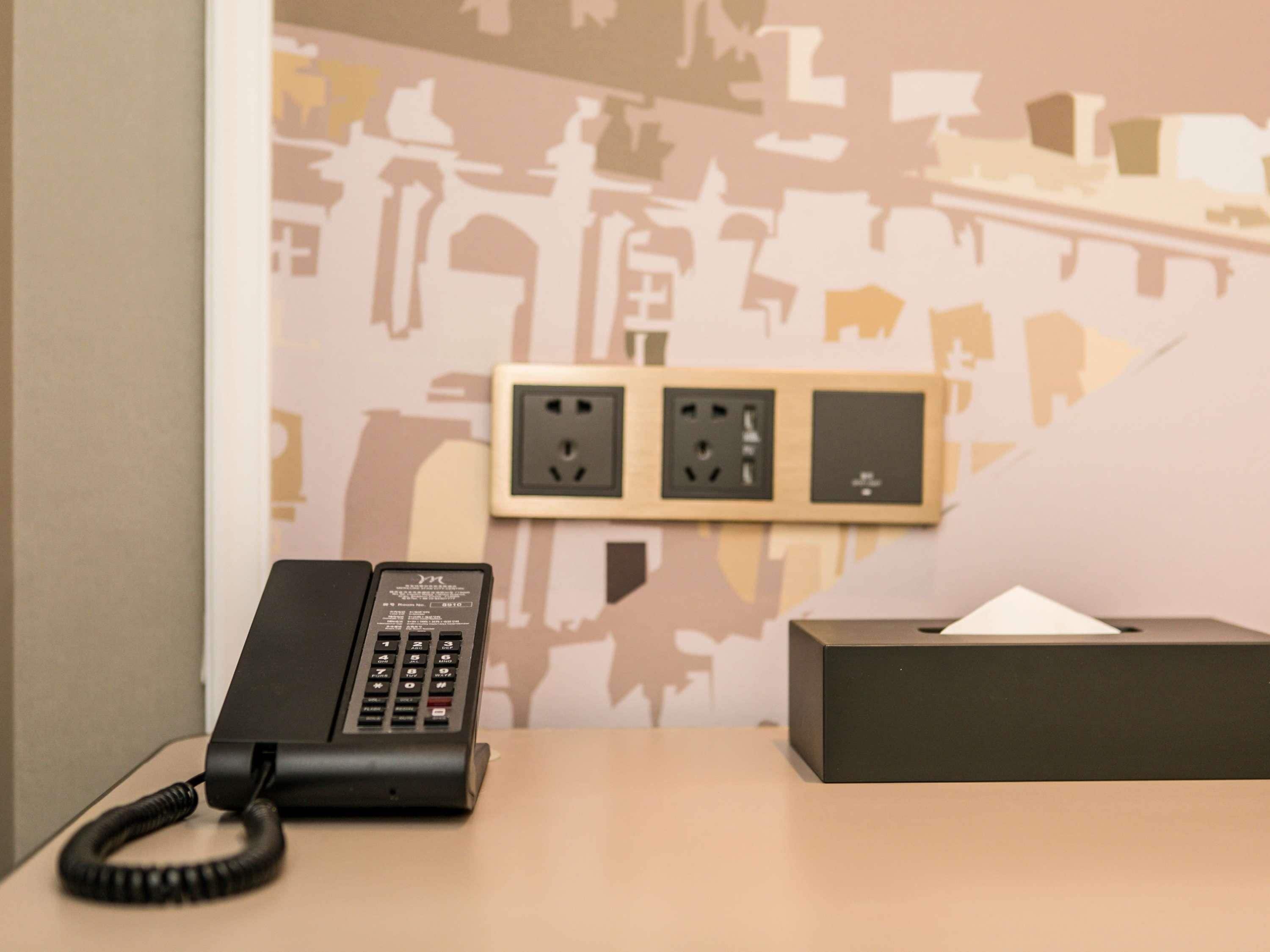A hotel room with a desk, a telephone, and a wall socket.