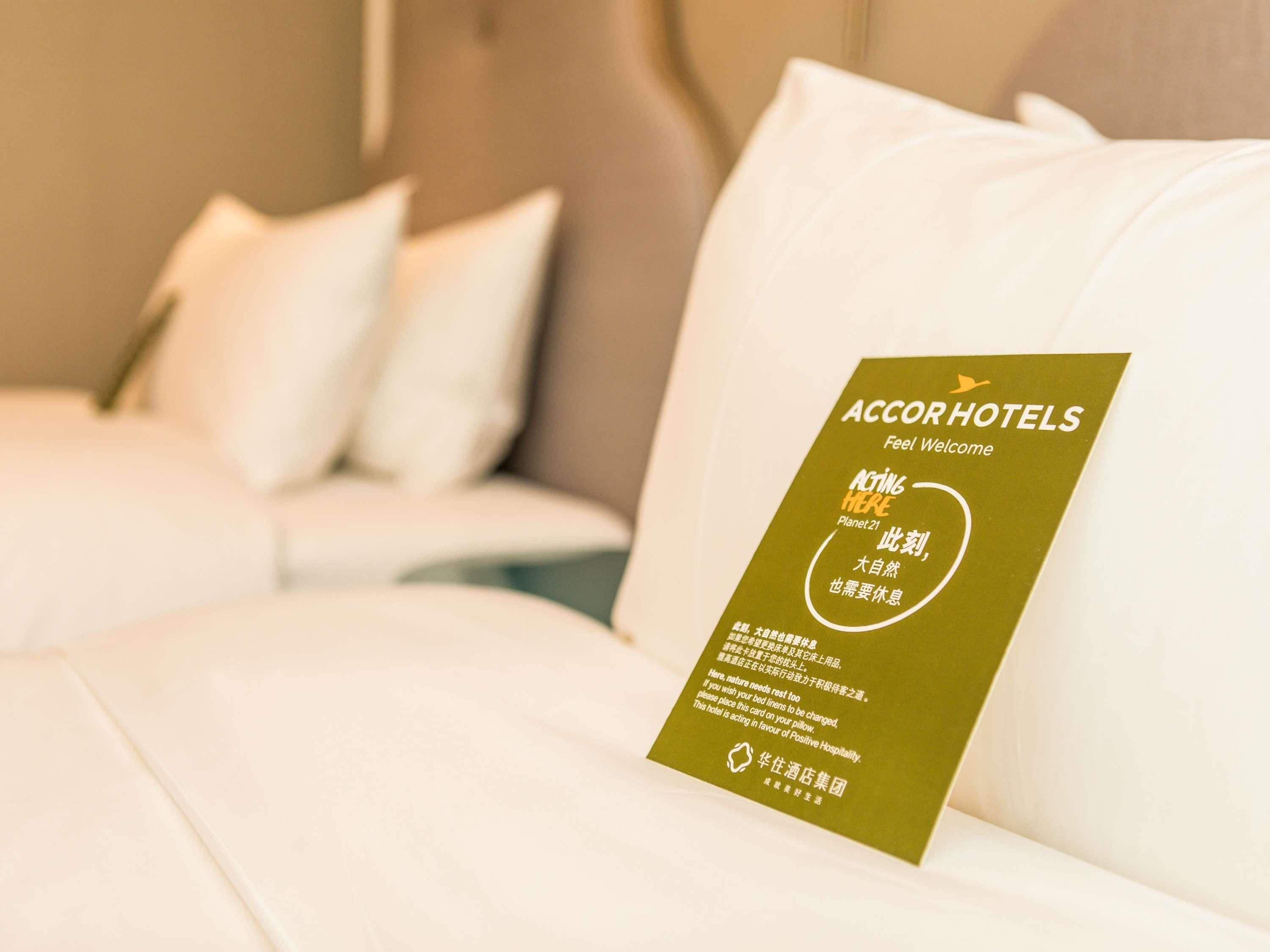 A hotel room with a neatly made bed and a sign on the headboard.