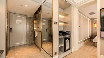 A hotel corridor with a mirrored wall, a glass elevator, a coffee machine, and a microwave.