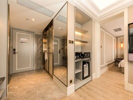 A hotel corridor with a mirrored wall, a glass elevator, a coffee machine, and a microwave.