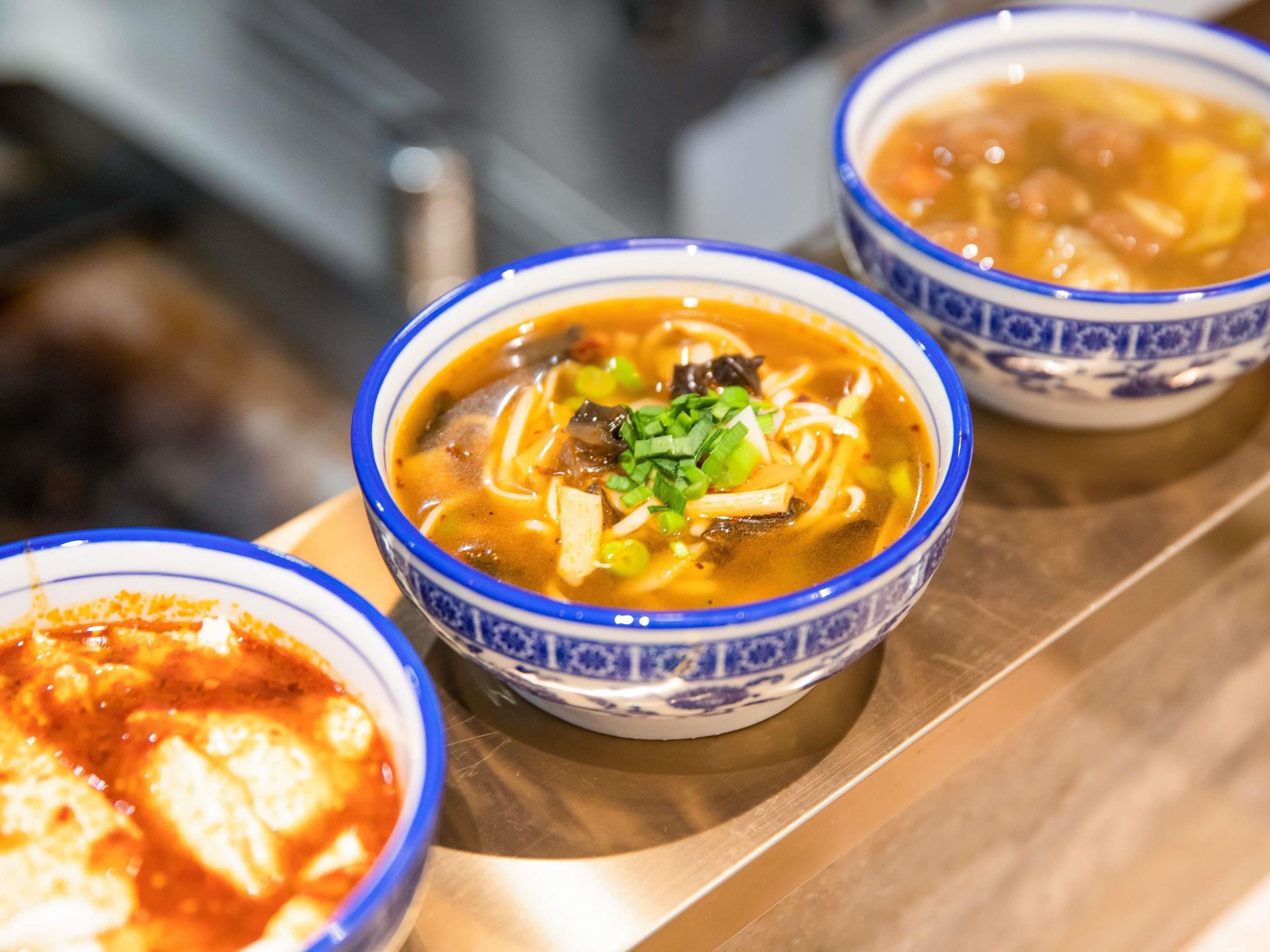 Three bowls of soup with noodles and vegetables on a tray.