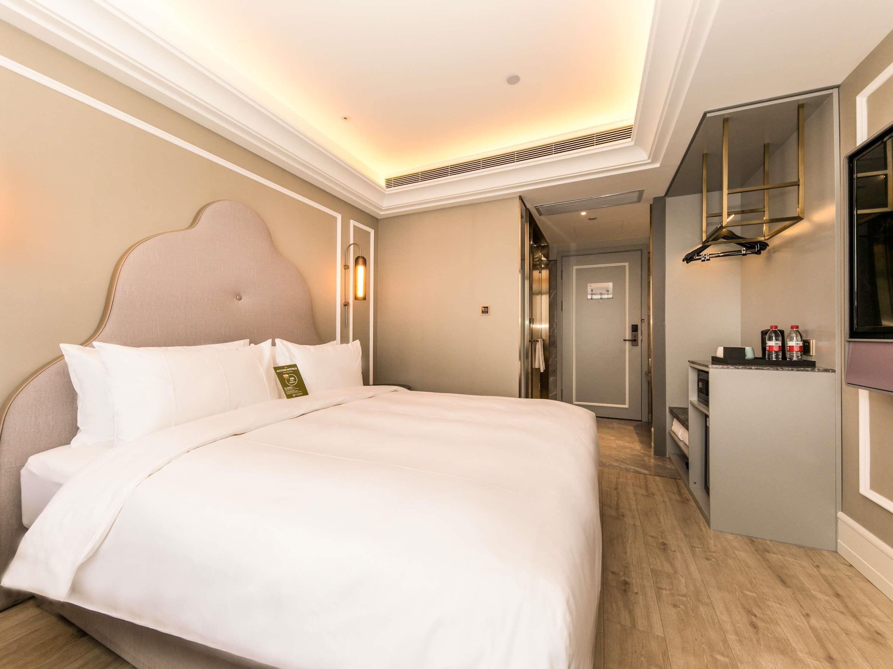 A hotel room with a large bed, a minibar, a television, and a bathroom visible through an open door.