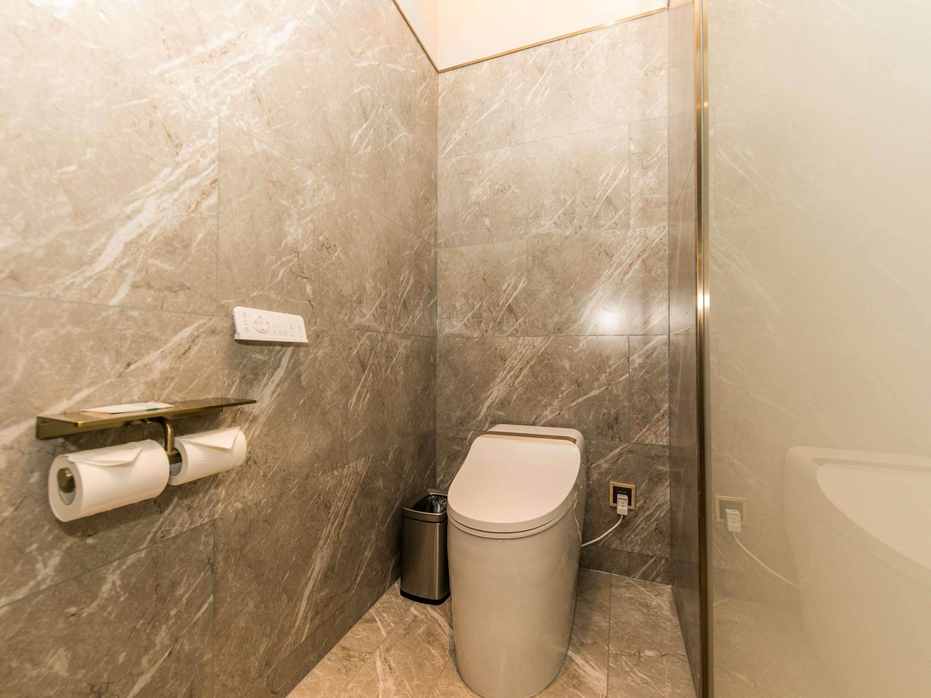 A modern bathroom with marble walls, a toilet, a trash can, and a toilet paper holder.