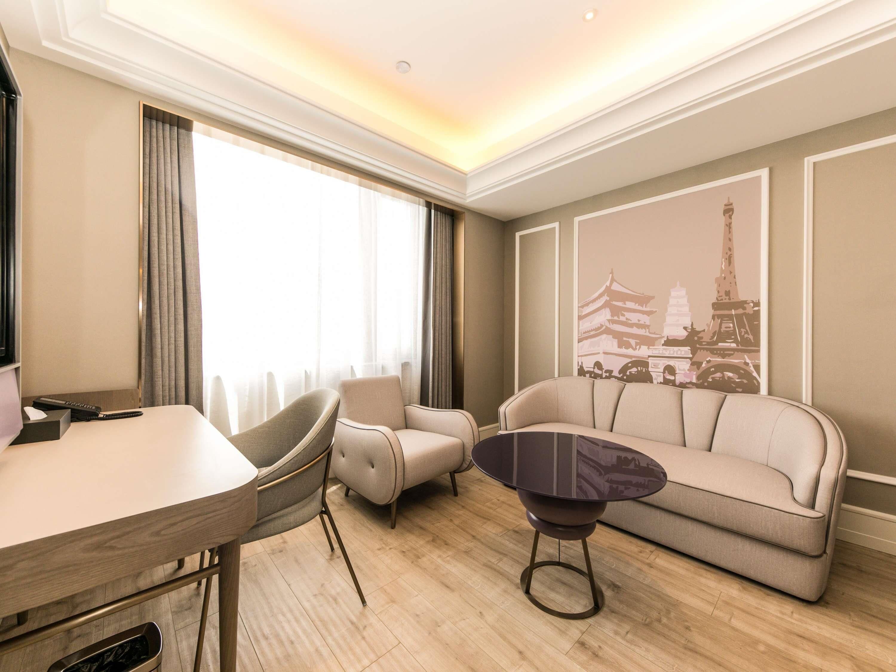 A modern hotel room with a dining area, a sofa, a coffee table, and a large window with curtains.
