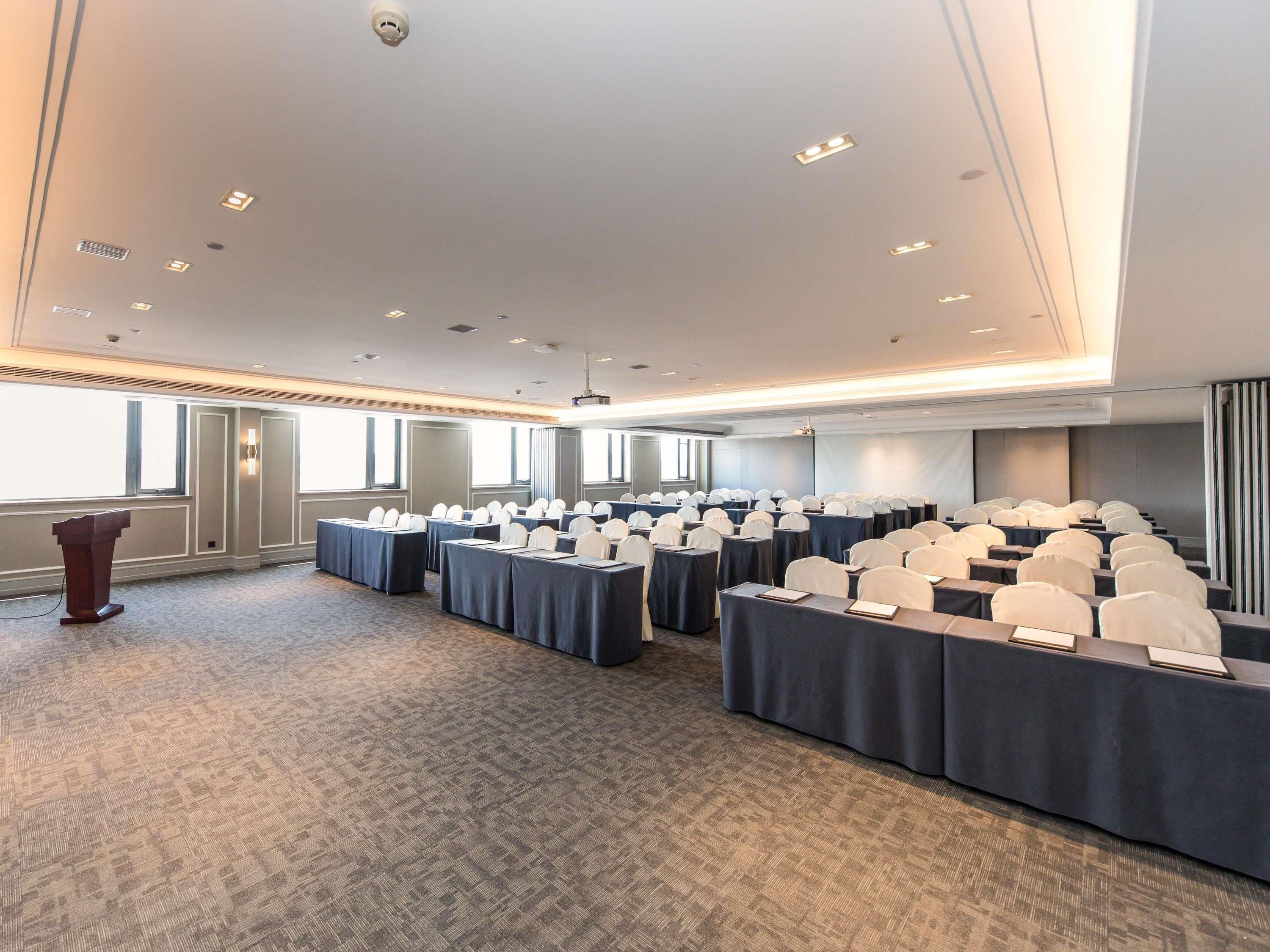 Un salón de conferencias con filas de mesas, sillas y un atril.