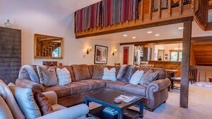 A spacious living room with a large sectional sofa, a coffee table, and a staircase with a colorful striped covering.
