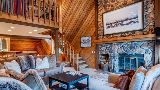 A cozy living room with a fireplace, leather sofas, and a wooden staircase.