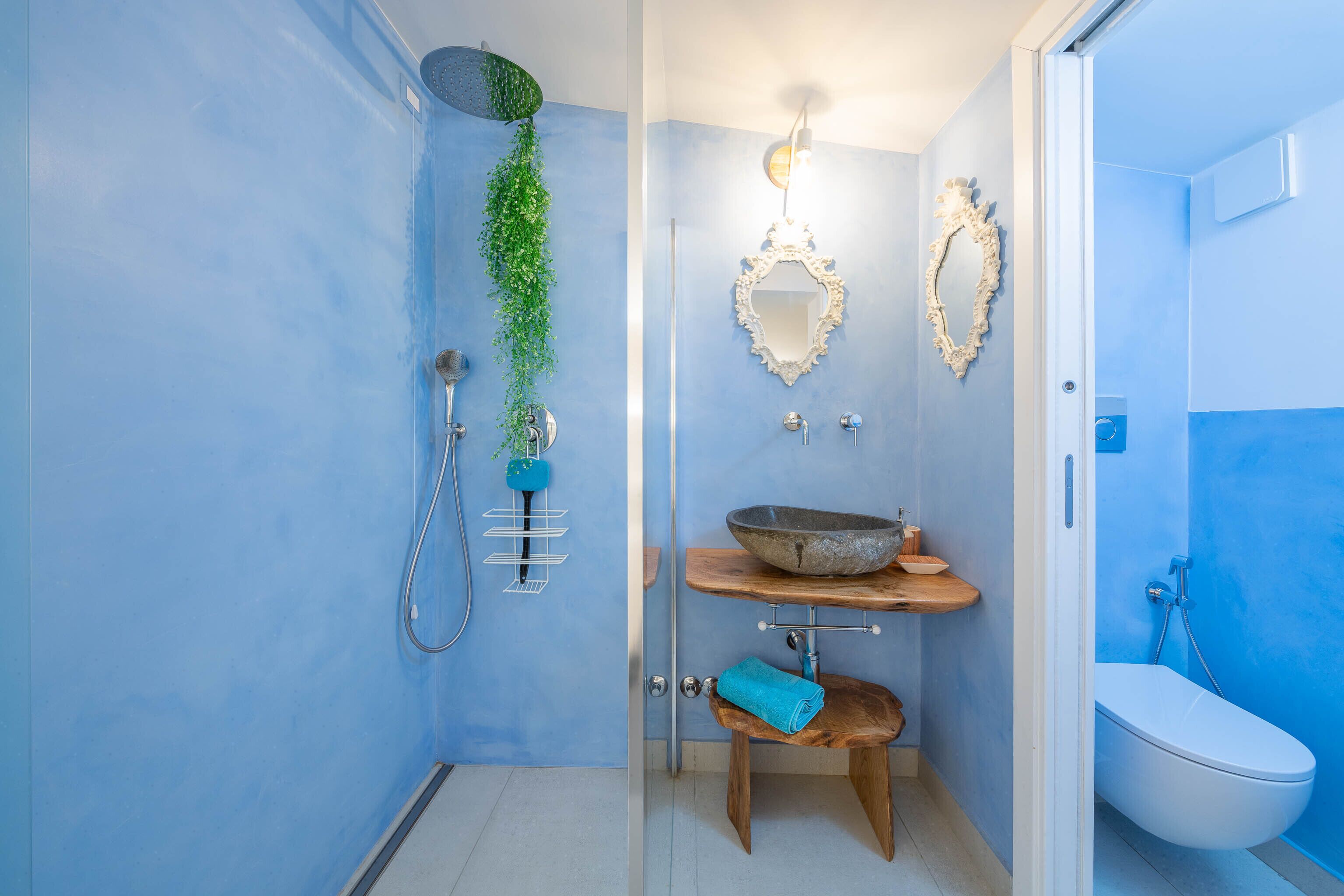A bathroom with a shower, a sink with a bowl, a mirror, and a towel on a stool.
