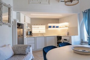 A compact kitchen with white cabinetry, a dining area with a round table, and a blue chair.