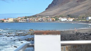 Une ville côtière avec des bâtiments qui bordent la plage, une plage rocheuse et une montagne en arrière-plan.