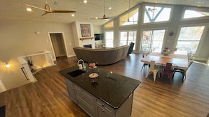 Una cocina amplia con una isla central, un comedor con mesa de madera y ventanas grandes que dejan entrar luz natural.